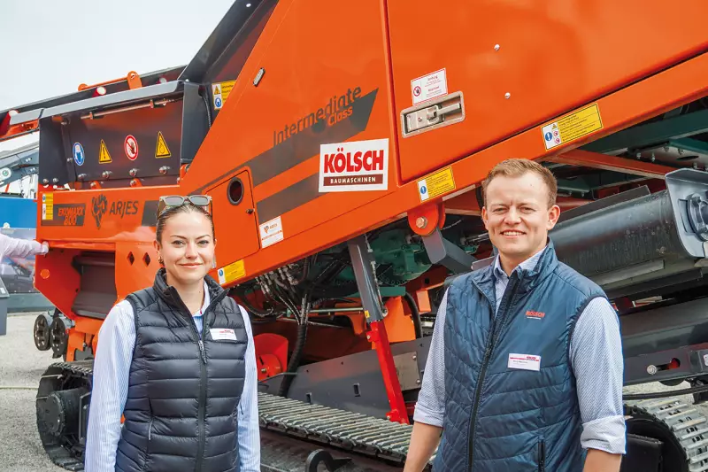 Die zweite Generation der Jürgen Kölsch GmbH: Paula und Philipp McCusker. Auf der IFAT zeigte Kölsch Präsenz an mehreren Partnerständen, darunter bei Arjes, Zemmler und Screenpod. Im Bild stehen beide am Arjes-Stand vor dem Ekomaxx 800, einem mobilen Zweiwellenzerkleinerer für u. a. Gewerbeabfälle, Grünschnitt, Altholz und Wurzeln. Quelle: Treffpunkt.Bau